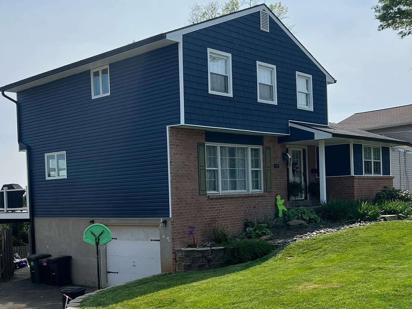 A large house with a blue siding and white trim is sitting on top of a lush green hill.
