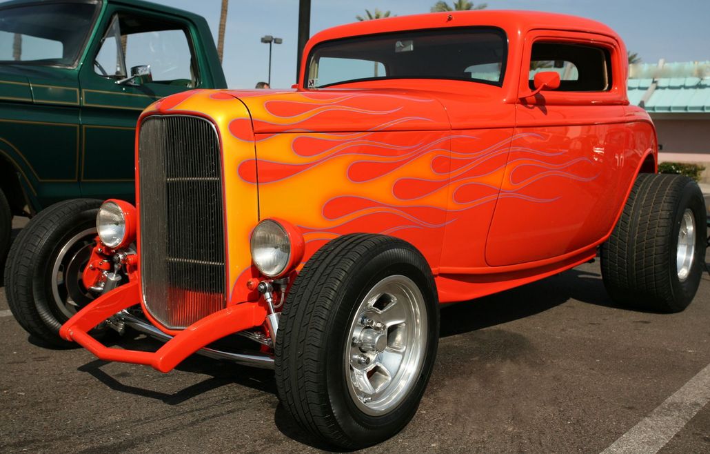 Bright orange flame-painted hot rod with chrome wheels parked outdoors