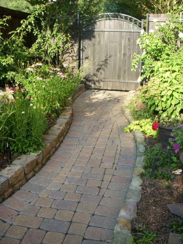 A brick walkway leading to a wooden gate in a garden