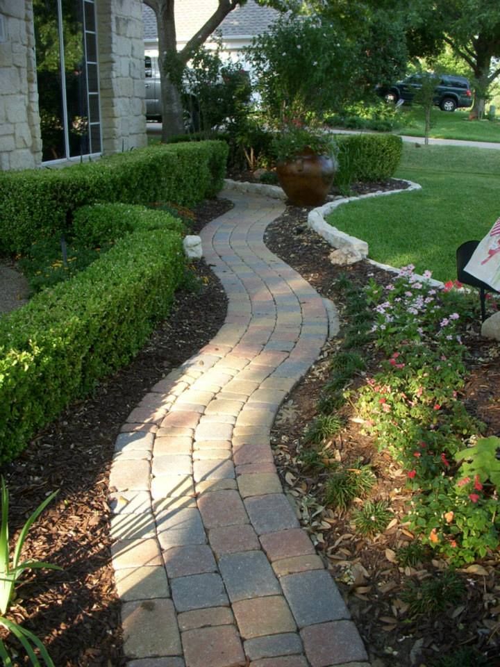 A brick walkway leading to a house in a garden