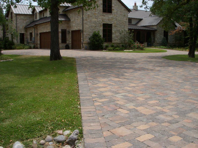 A brick driveway leading to a large stone house