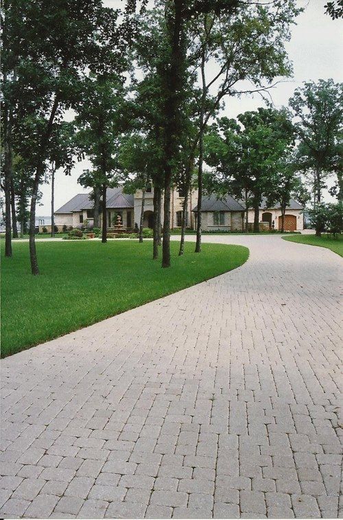 A brick driveway leading to a house with trees on both sides
