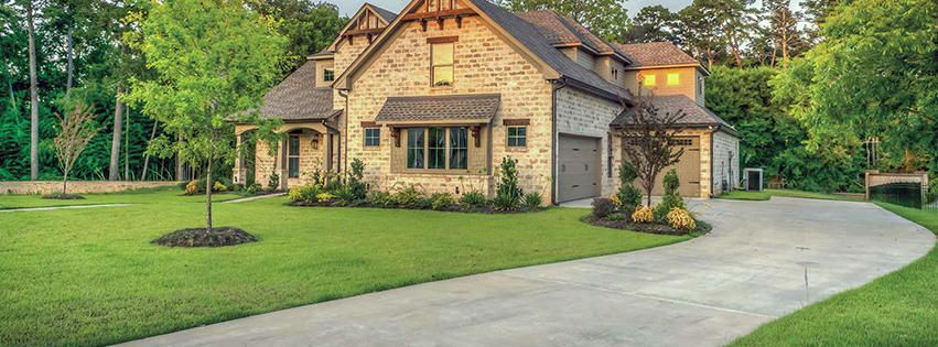 A large house with a long driveway leading to it is surrounded by trees.