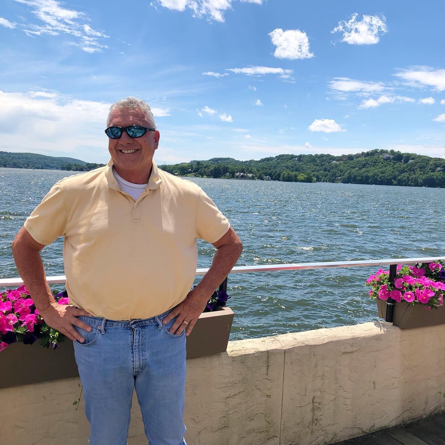 A man wearing sunglasses is standing in front of a body of water.