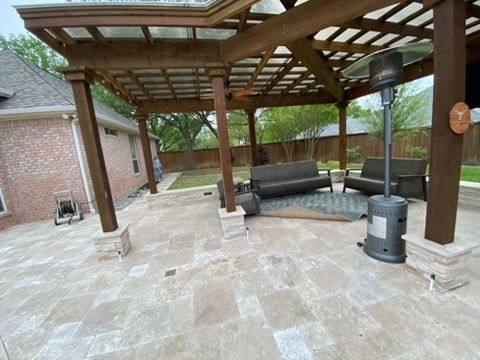 A patio with a pergola , couch , chairs and a heater.
