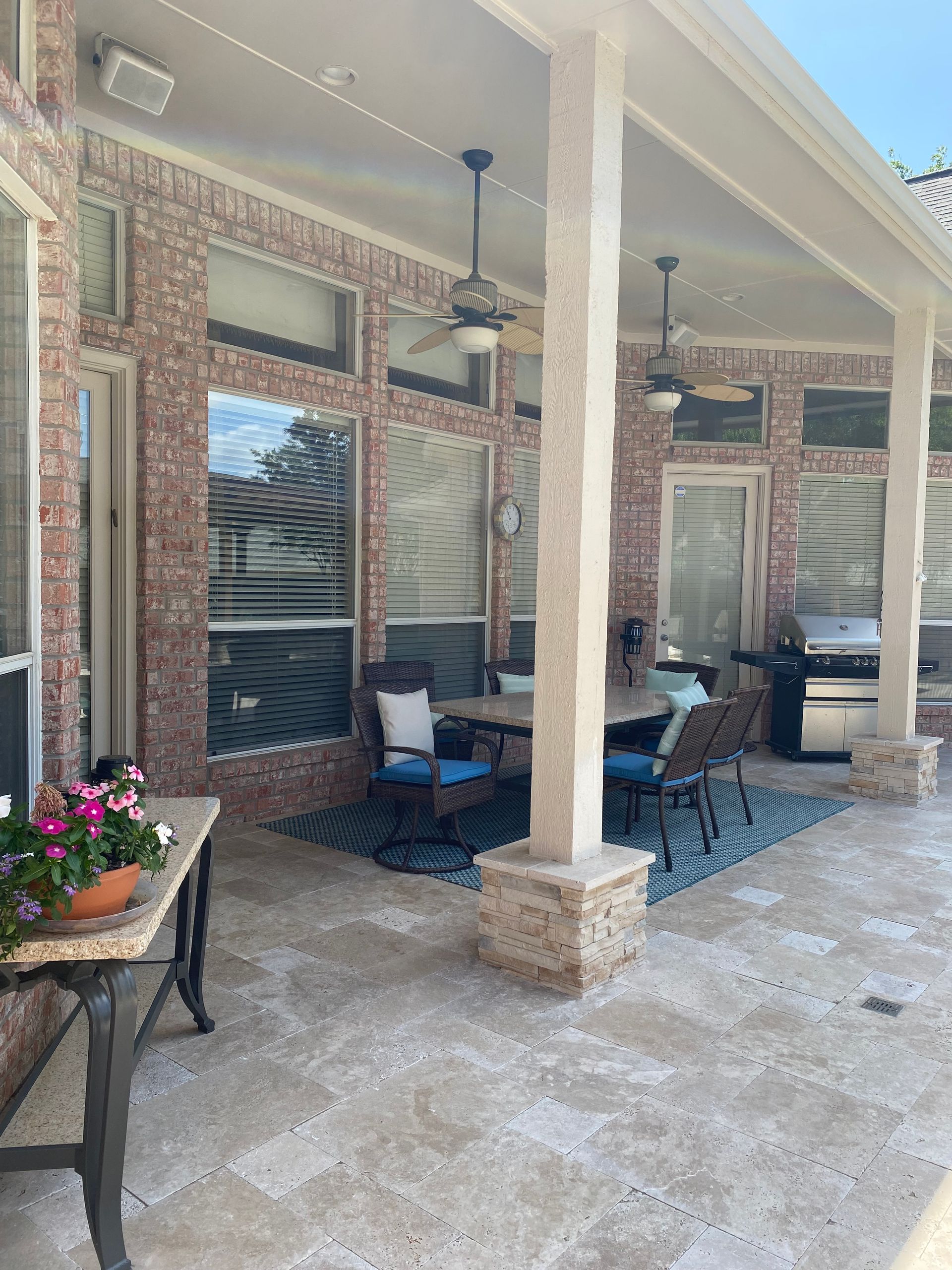 A patio with a table , chairs , a grill and a ceiling fan.