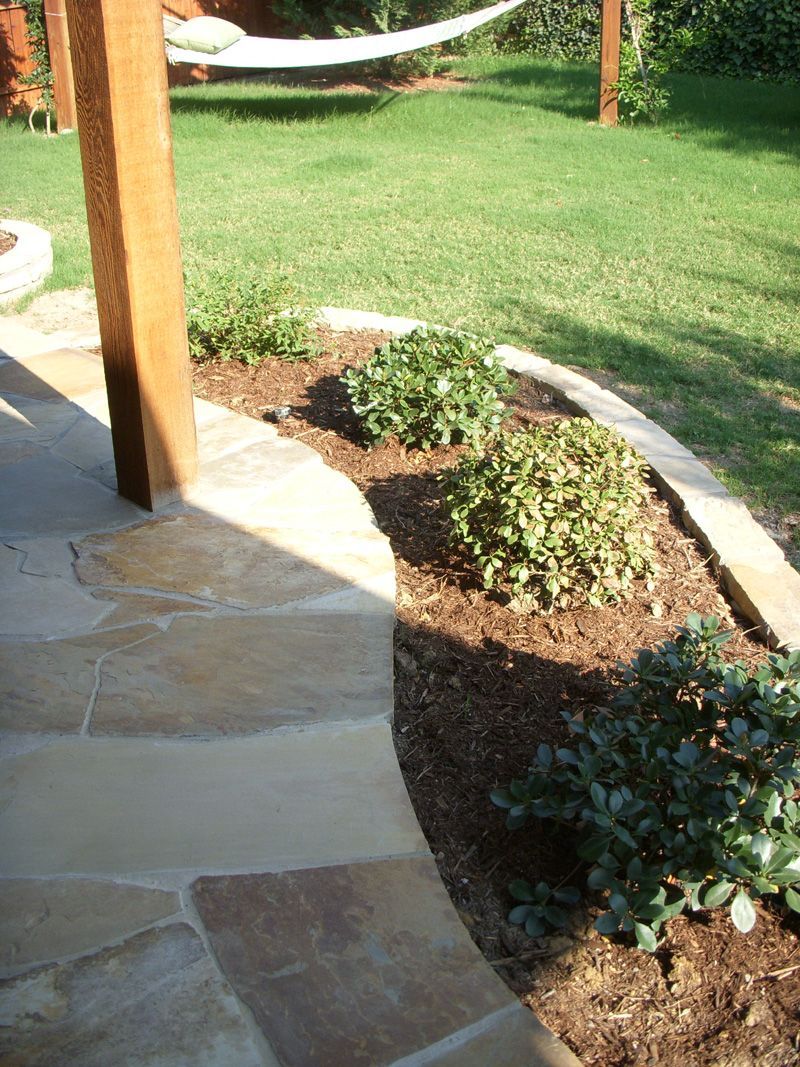 a hammock is sitting on top of a lush green lawn next to a stone walkway .