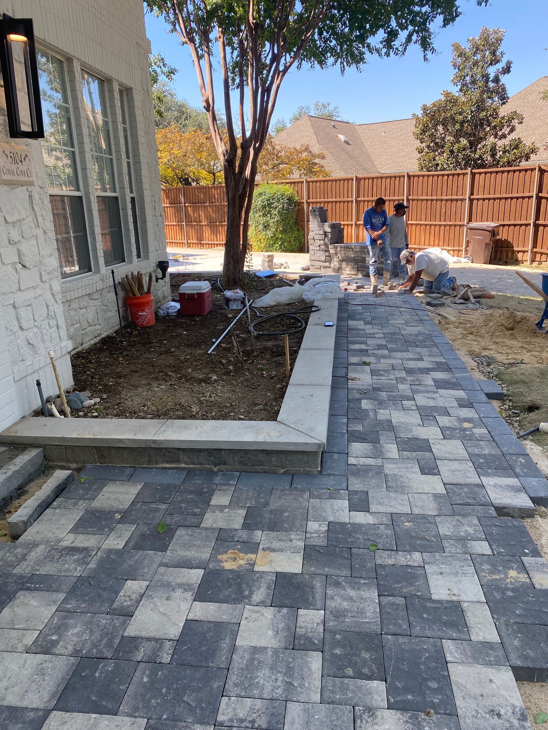 A group of people are working on a brick walkway in front of a house.