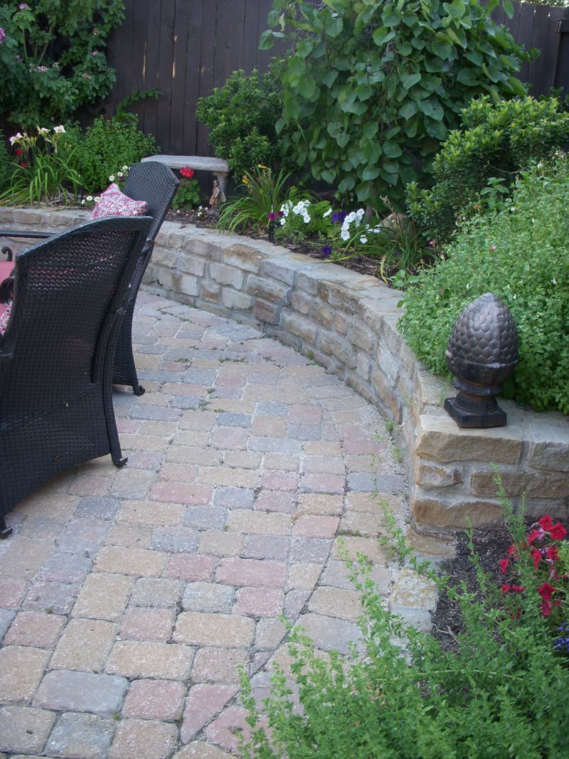 a patio with wicker chairs and a stone wall surrounded by plants .