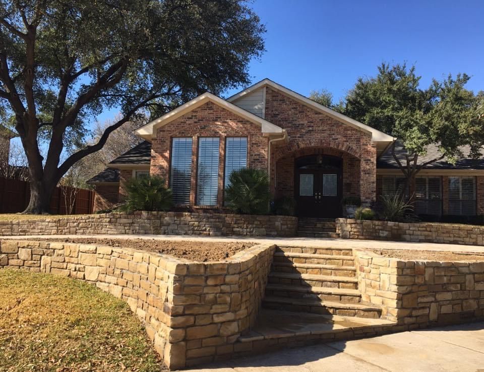 A brick house with a stone wall and stairs in front of it.