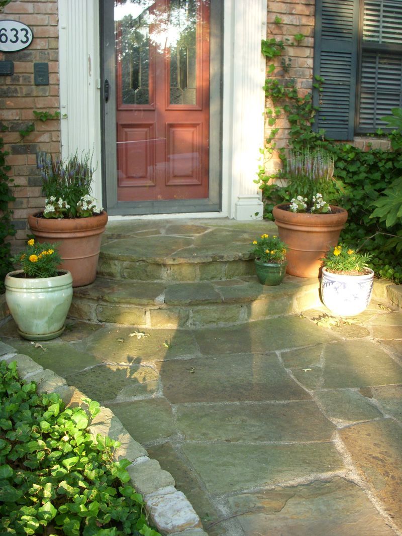 a stone walkway leading to a red door with potted plants in front of it .