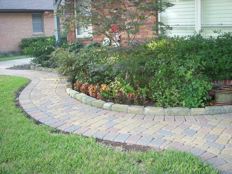 a brick walkway leading to a house with a garden in the background .