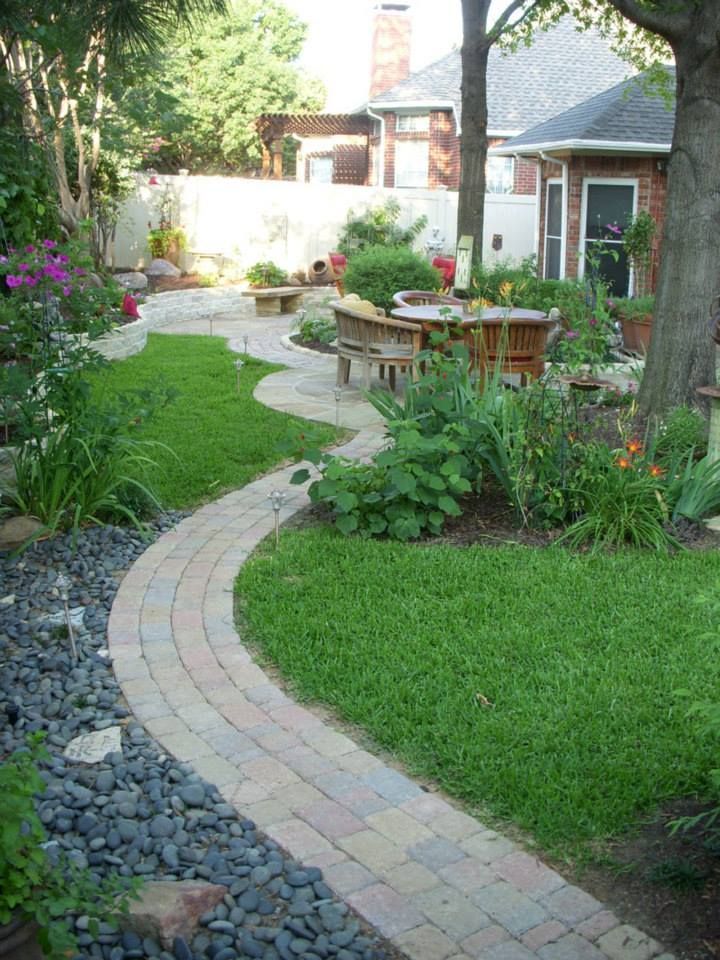 a backyard with a brick walkway leading to a table and chairs .