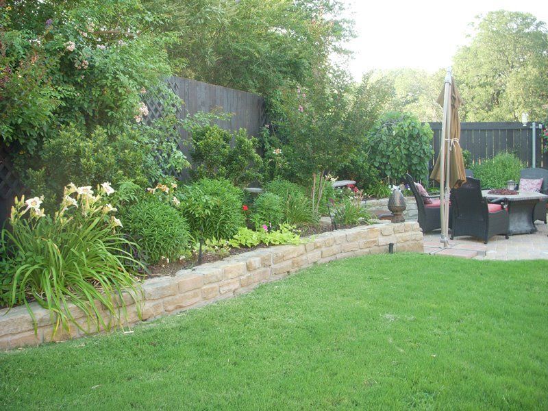 a lush green backyard with a stone wall and a patio area .