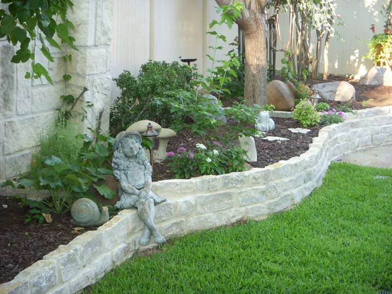 a statue of an angel is sitting on a stone wall in a garden