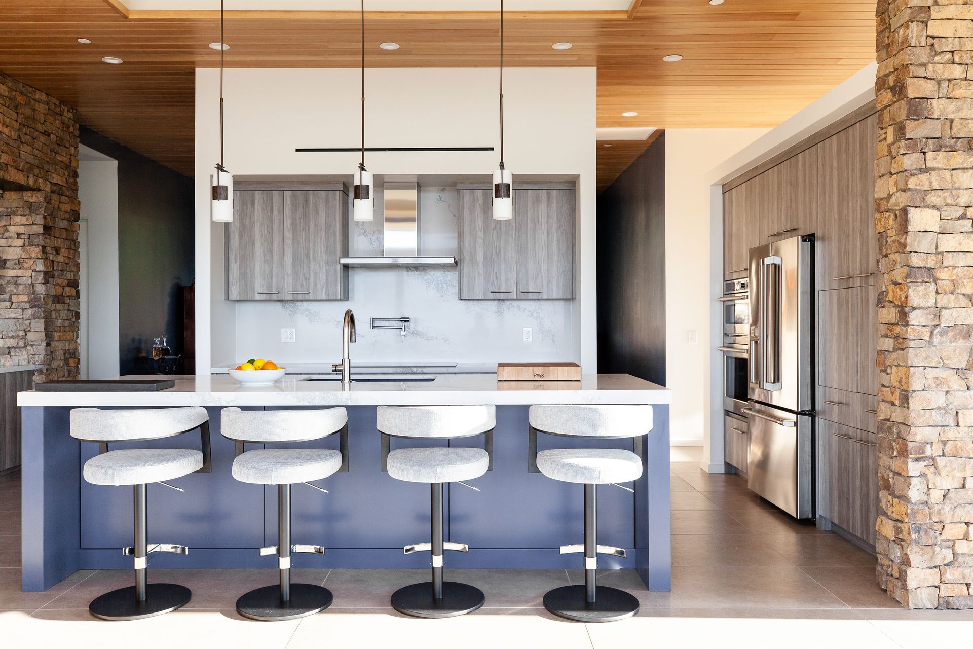 A kitchen with a large island, stools and a refrigerator.