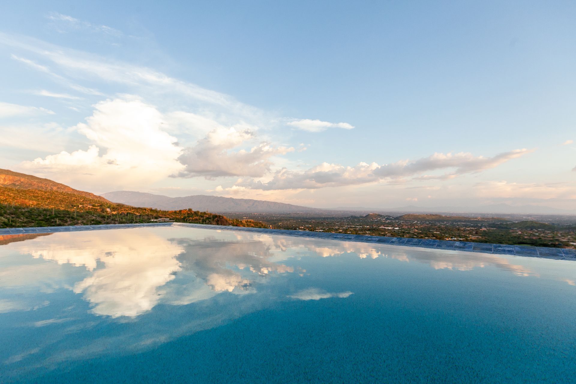 A swimming pool with a view of mountains and clouds reflected in the water.