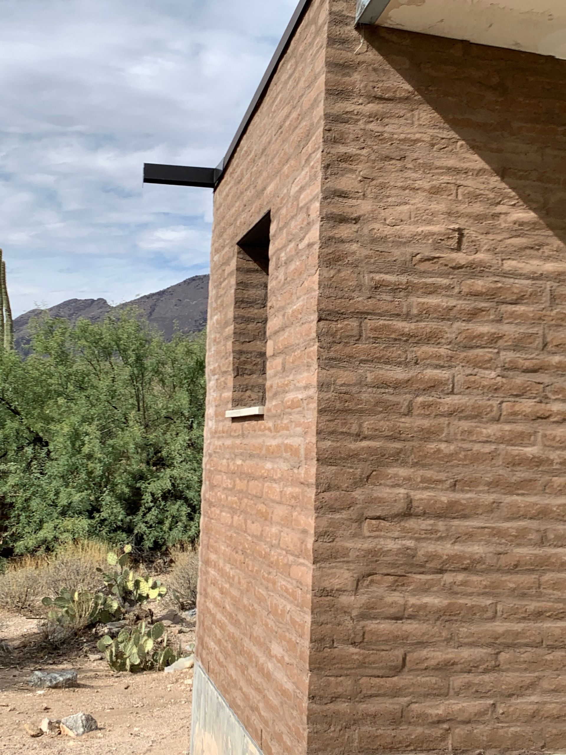 A brown brick building with a window and mountains in the background.