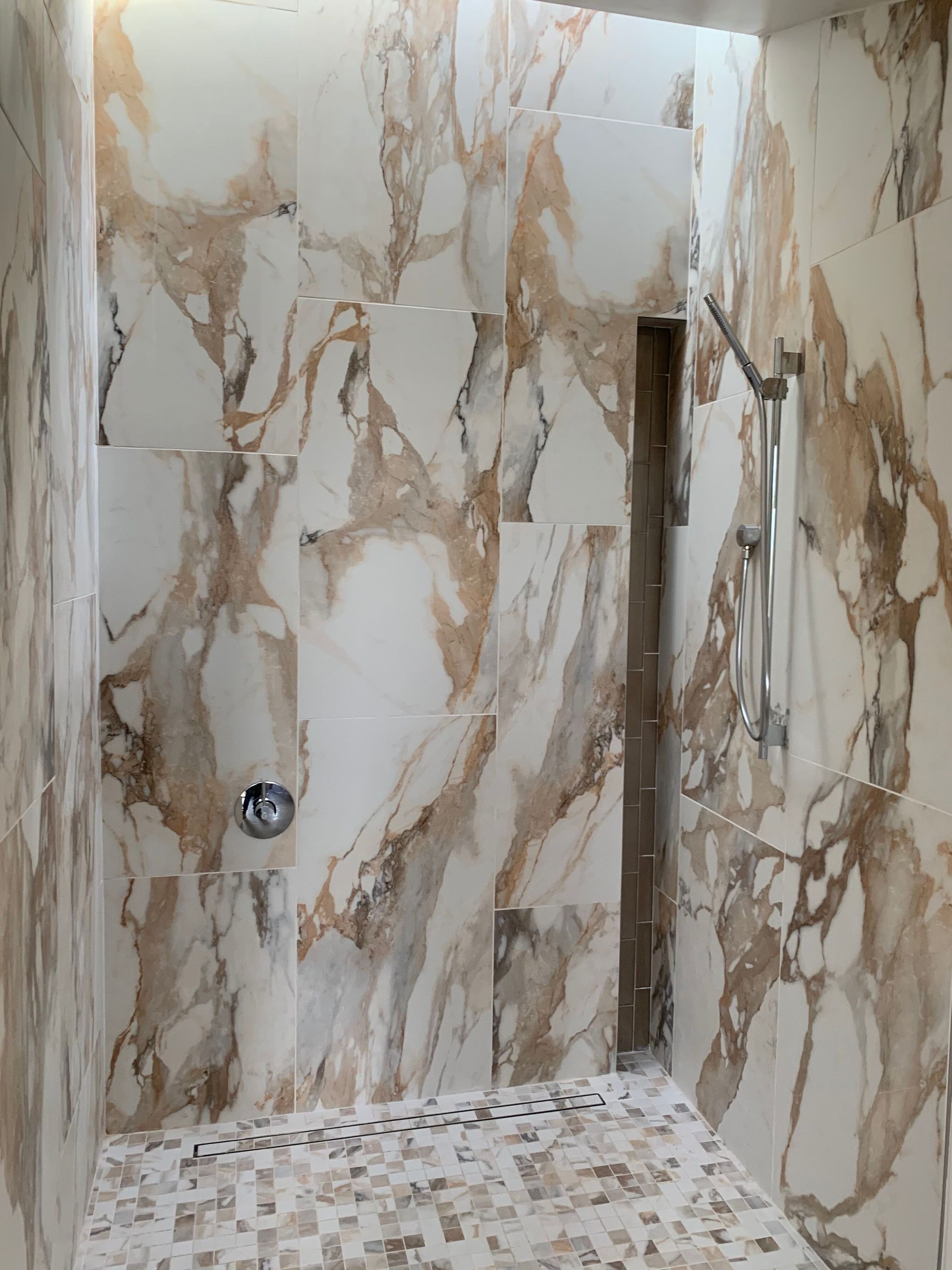 A bathroom with marble walls and tiles and a walk in shower.