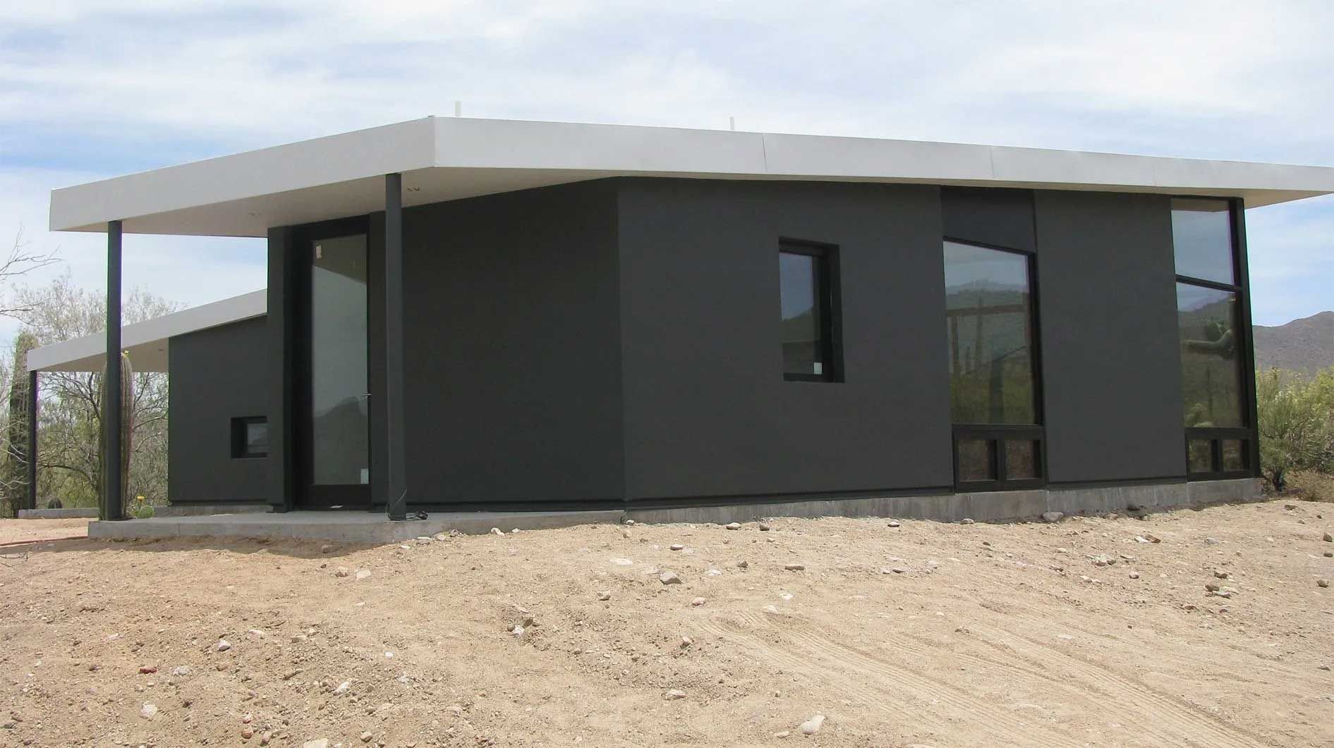 A small black house is sitting on top of a dirt hill.