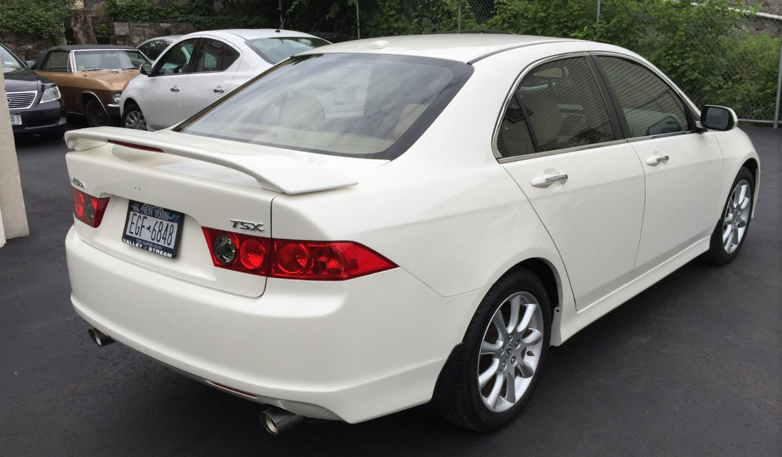 White sedan parked in a lot, rear three-quarter view, with red taillights and chrome wheels