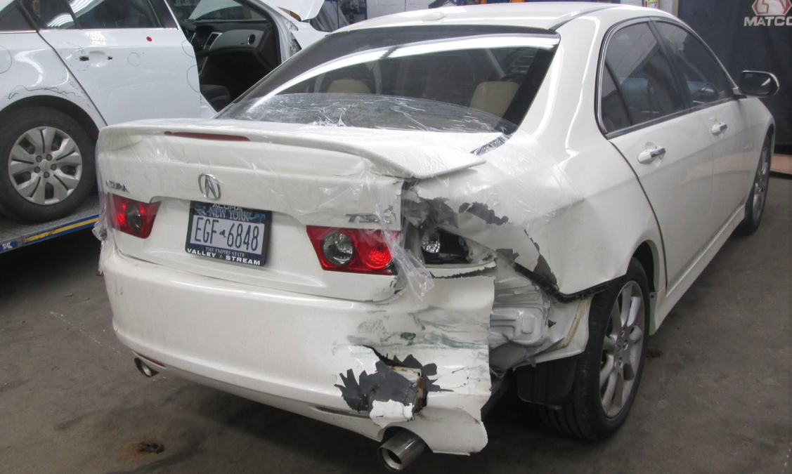 Silver sedan with severe rear-right damage in a parking lot, trunk and bumper crushed