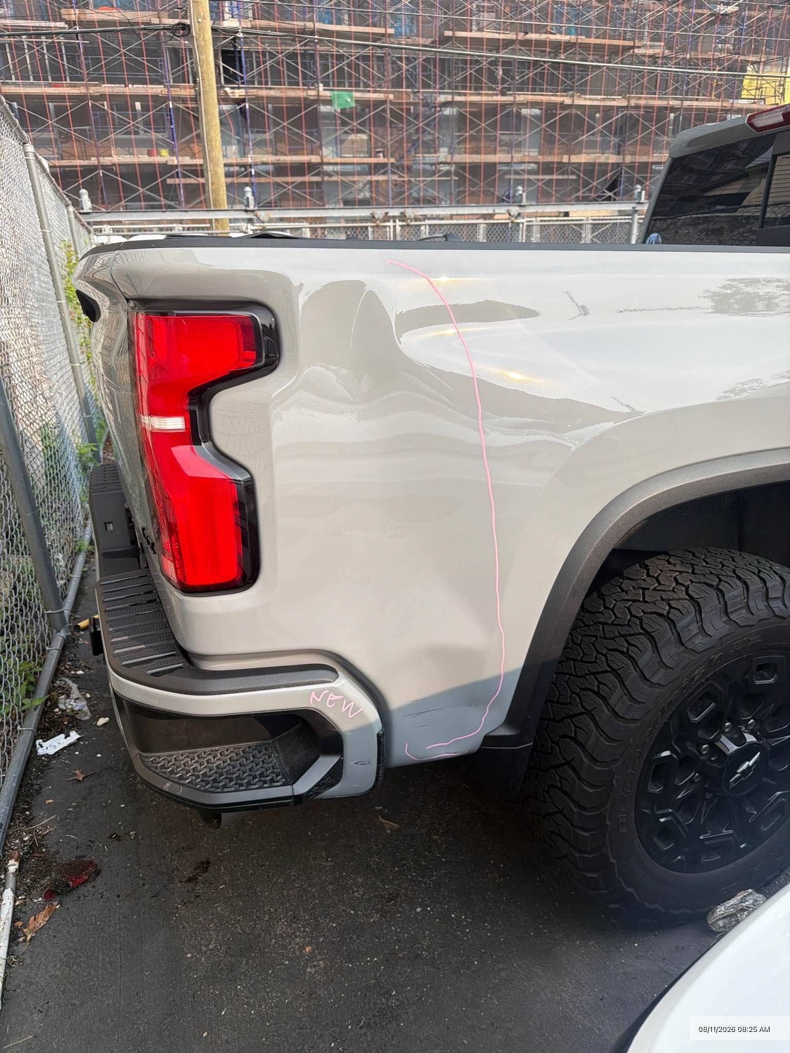 Close-up of a white pickup truck’s rear side and taillight beside a wall, with a black off-road tire visible