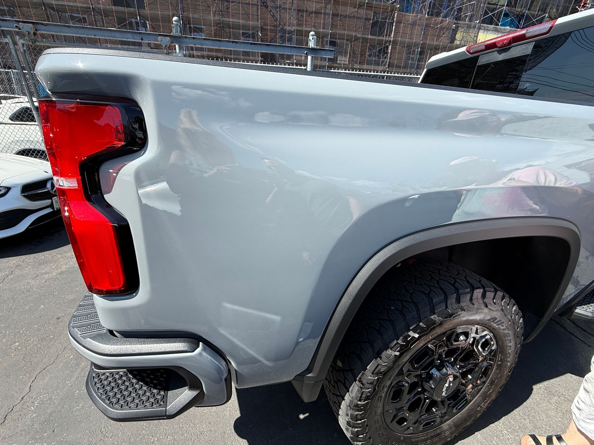 Gray pickup truck rear side with red taillight and black wheel in a parking lot