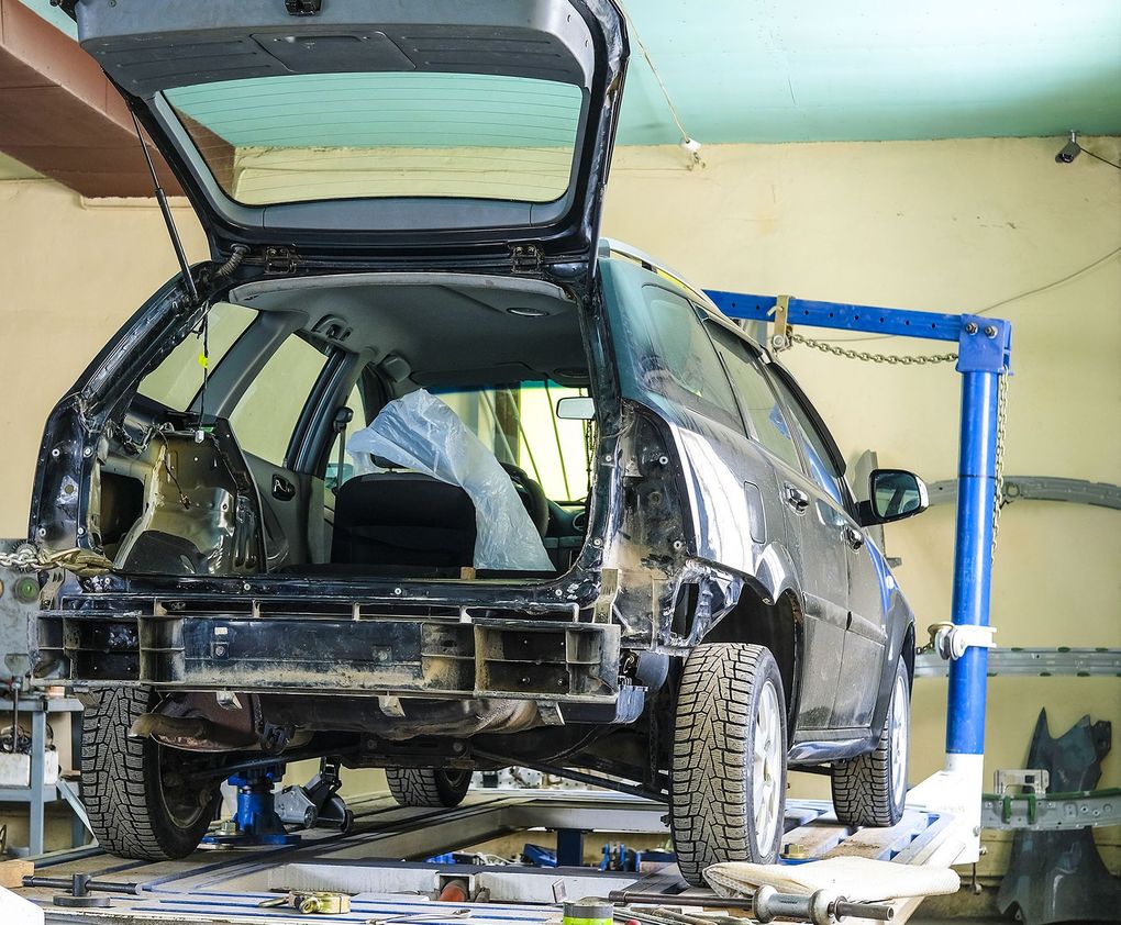 Damaged black SUV in a repair shop with rear hatch open and bodywork exposed on a lift