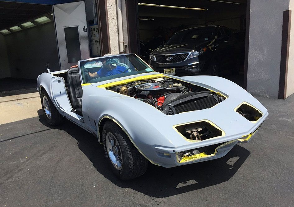 White classic sports car with its hood open, parked outside a garage.