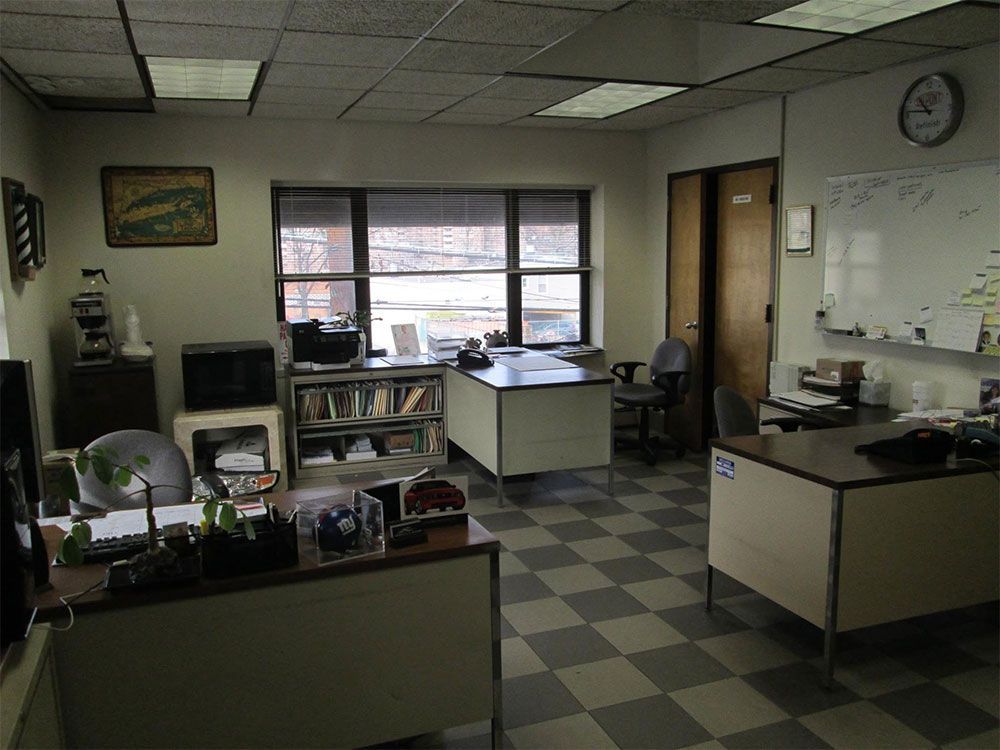 Empty office with desks, computer, bookshelves, windows, and a checkered floor.