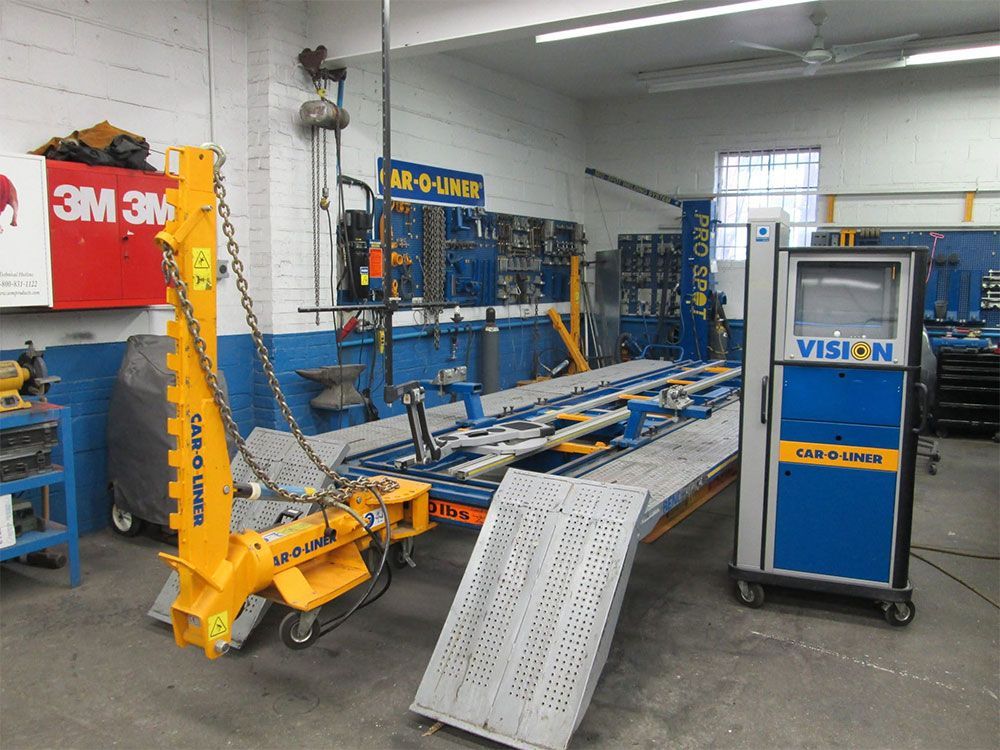 Industrial workshop with blue machine parts, yellow crane, and metal ramp in a garage setting