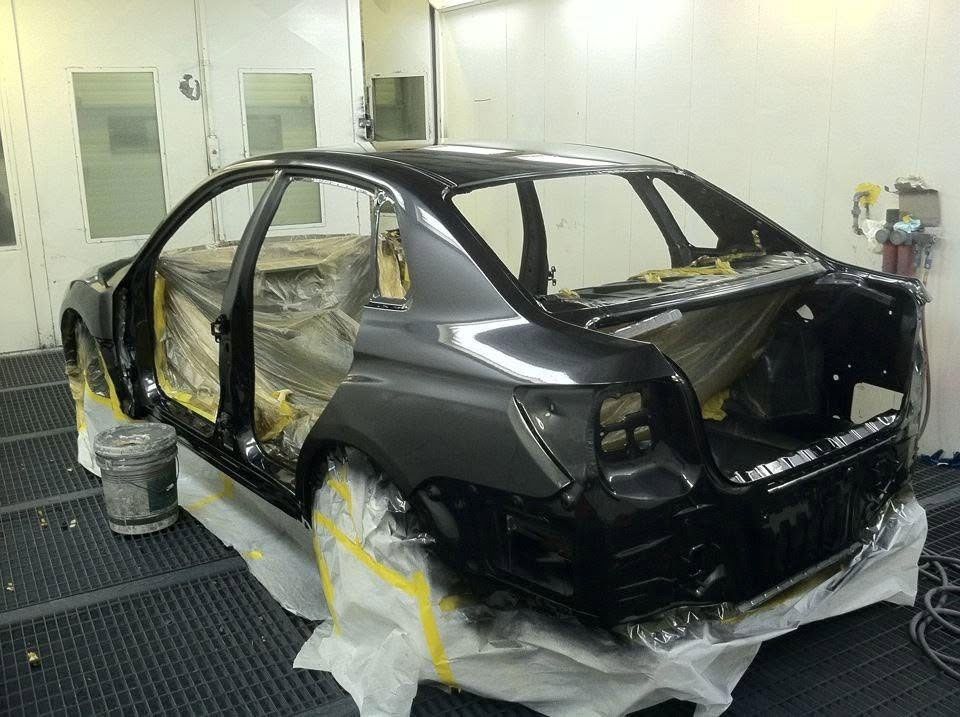 Black sedan in a body shop, partially disassembled and masked with tape and plastic for repainting.