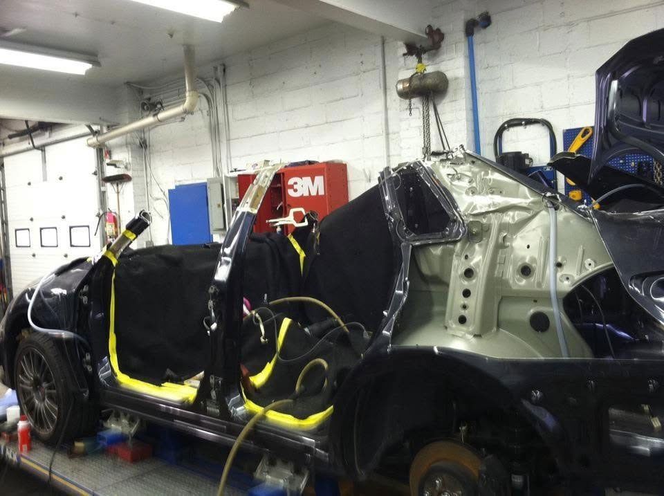 Damaged black car in a workshop, with exposed frame and repair equipment attached