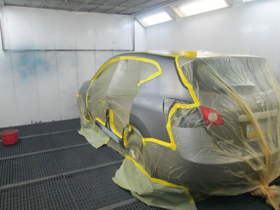Car wrapped in plastic and yellow tape inside a white spray booth, ready for painting