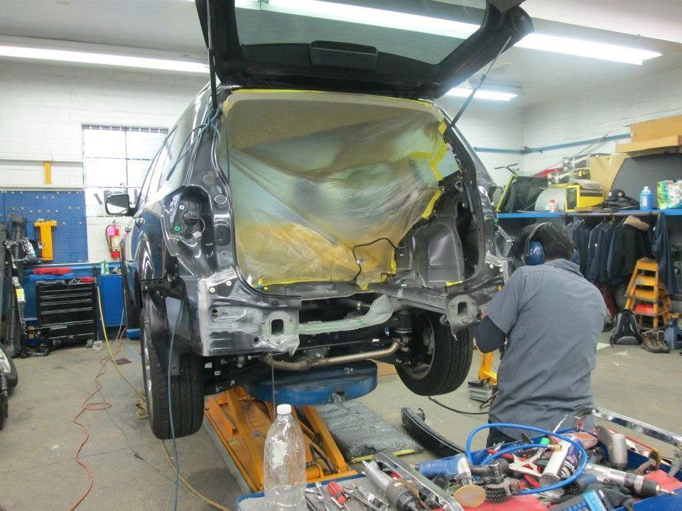 Car damaged in an auto shop, with the rear heavily crushed and a mechanic working nearby.