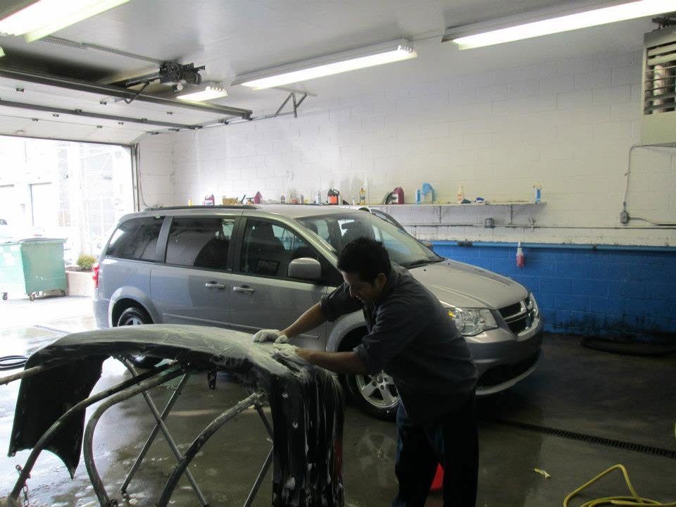 Mechanic polishing a minivan in a garage beside a car in the foreground