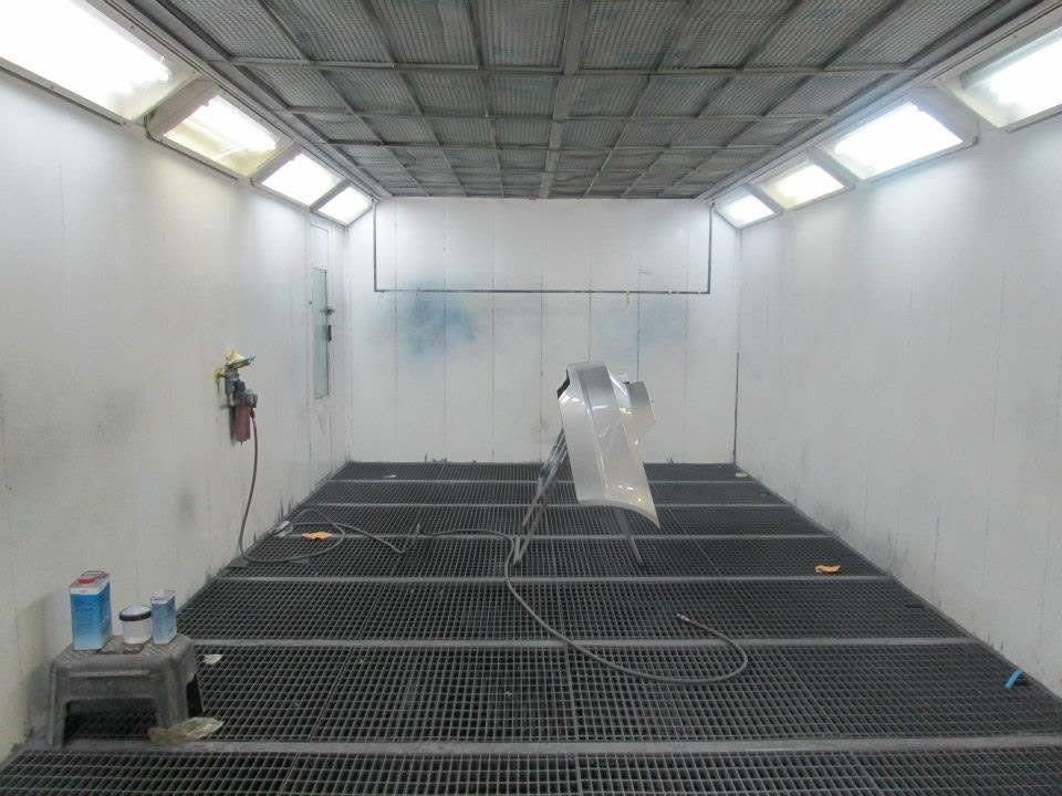 Empty industrial spray booth with grated floor, overhead lights, and a plastic-covered object in the center