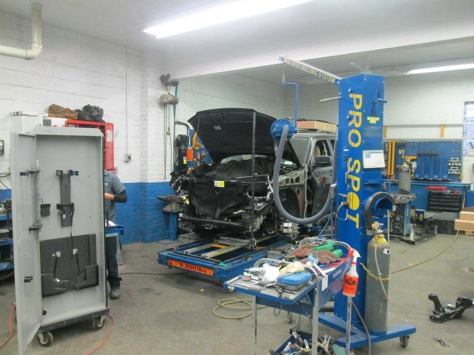 Auto repair shop with a car on a lift, open hood, and blue diagnostic equipment near a workbench.