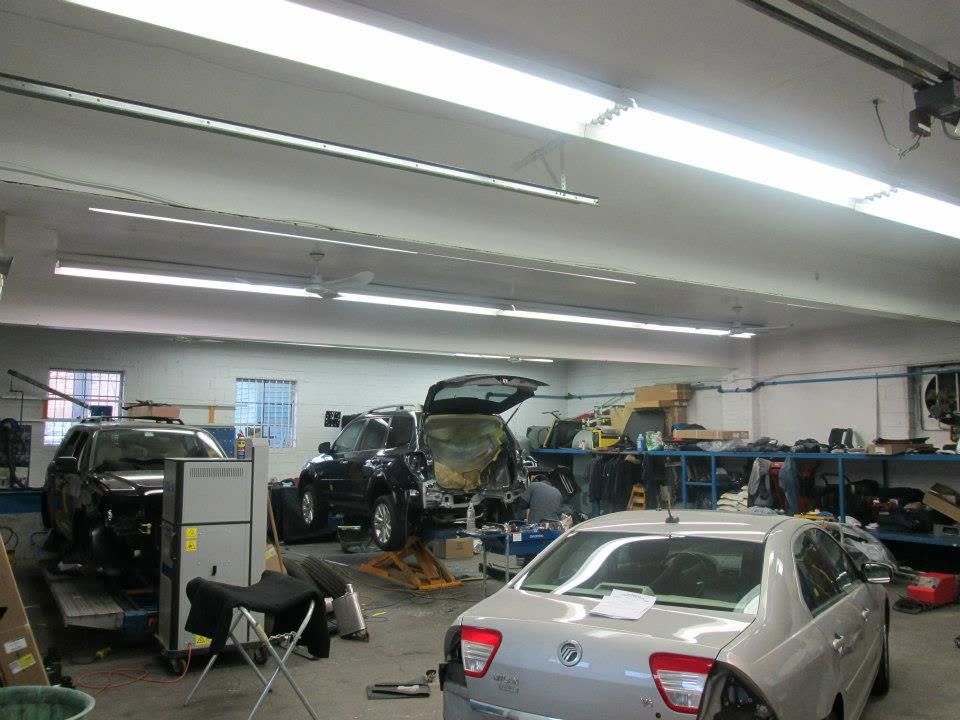 Auto repair shop with several cars, mechanics, and equipment under bright overhead lights.