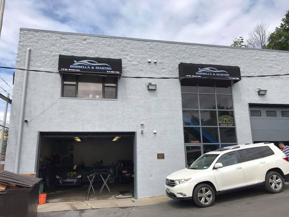 Gray auto repair shop exterior with open garage bay and a white SUV parked outside