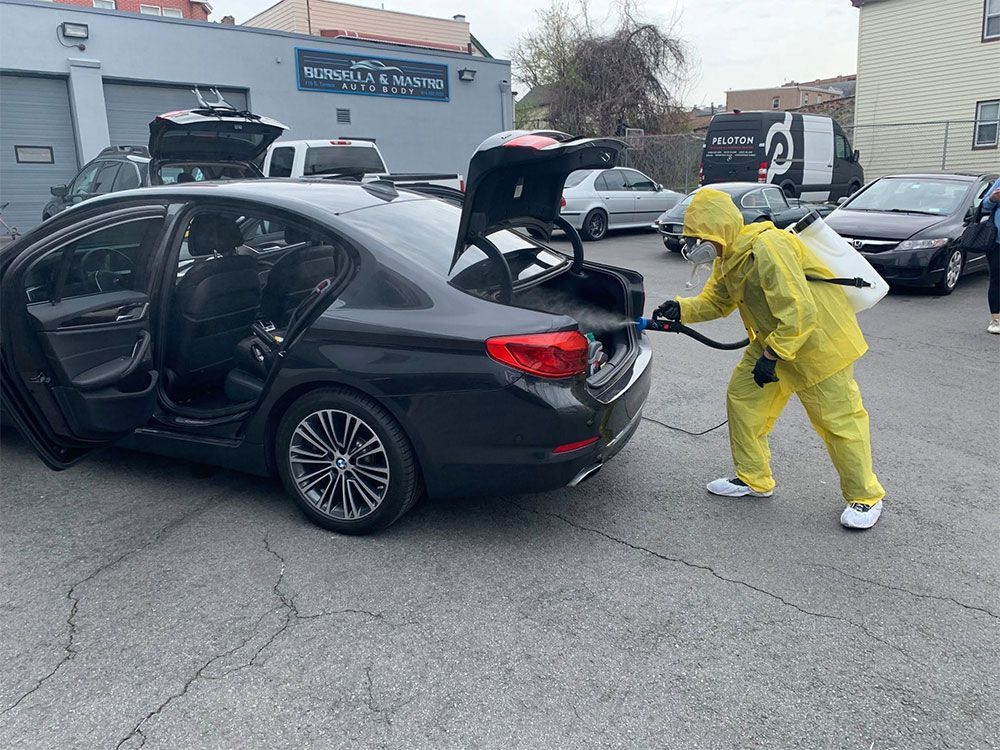 Person in yellow hazmat suit disinfects black sedan in parking lot