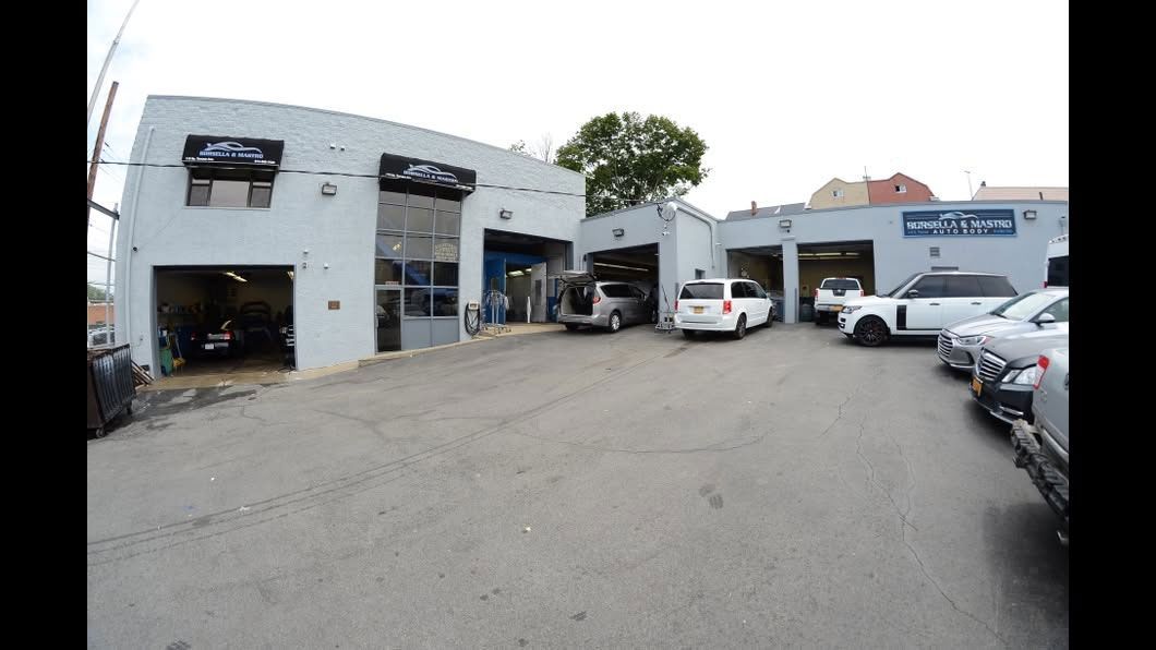 Auto repair shop parking lot with several cars outside a white industrial building.