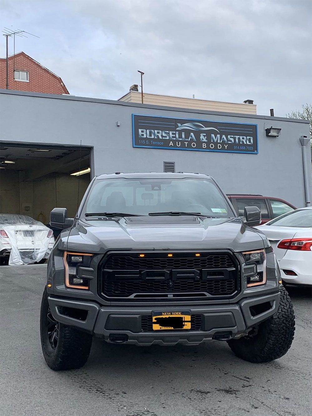 Front view of a gray pickup truck parked outside a building with other vehicles nearby.