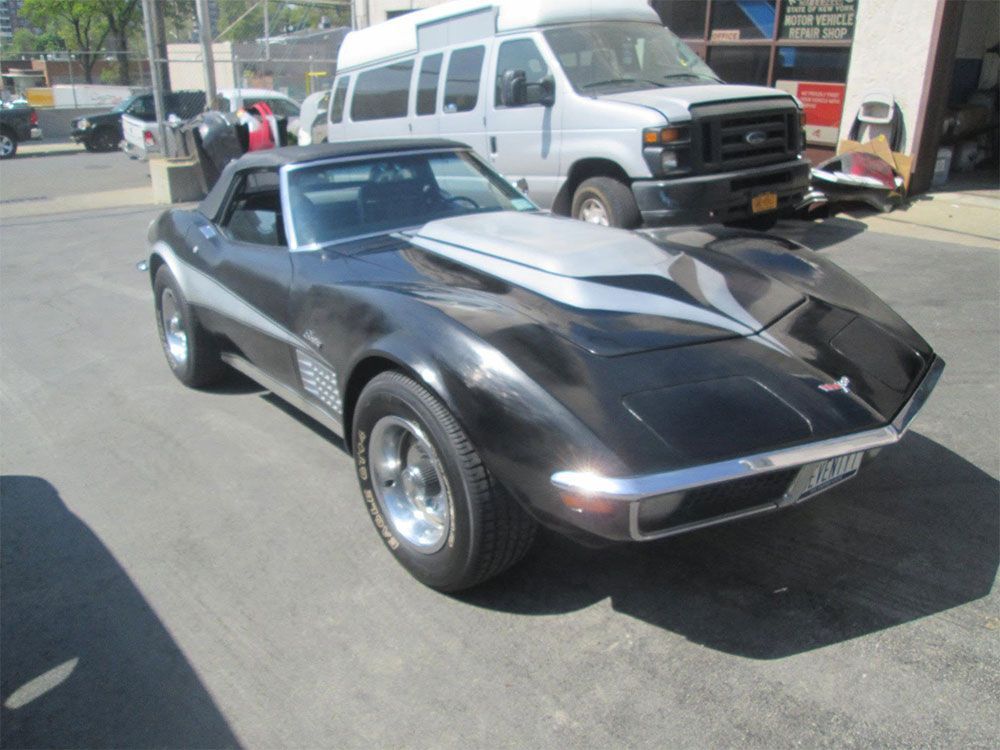 Black classic Chevrolet Corvette convertible parked on a street beside a white van