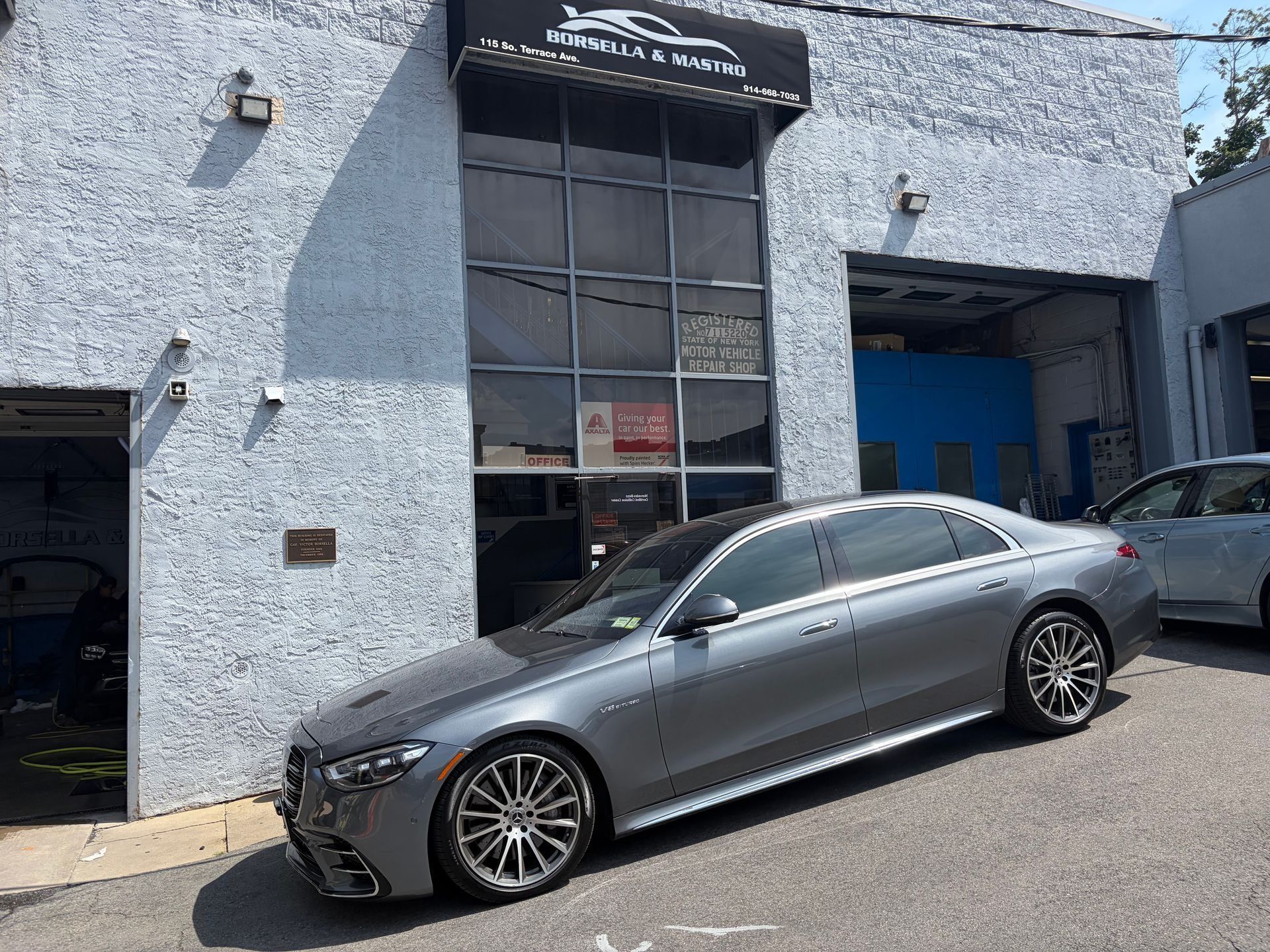 Car parked outside a light-blue auto shop with an open garage door