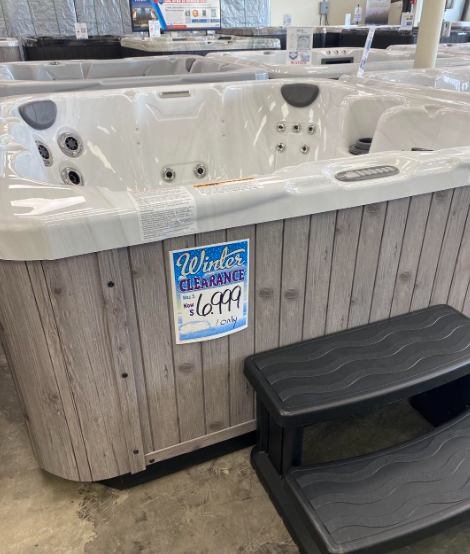 A white hot tub with grey wood paneling on a showroom floor, featuring a 