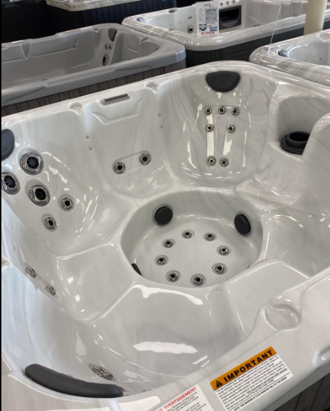 A white, multi-seat hot tub with numerous jets and gray headrests, shown from a high-angle view in a showroom.