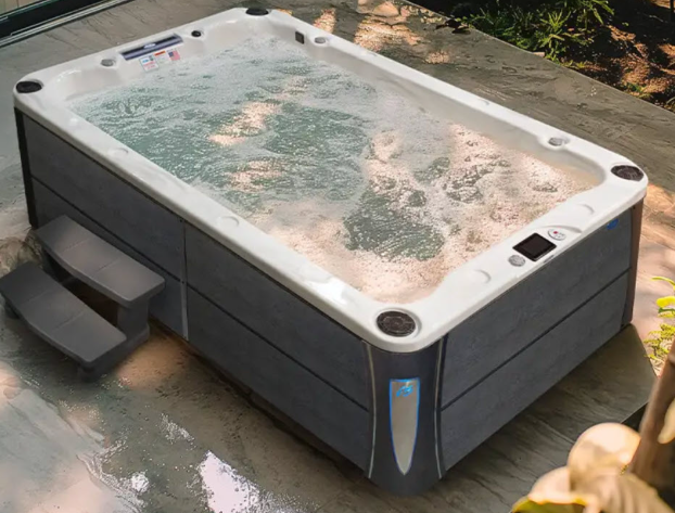 A rectangular hot tub with dark gray siding, white interior, and bubbling water, positioned outdoors with entry steps.