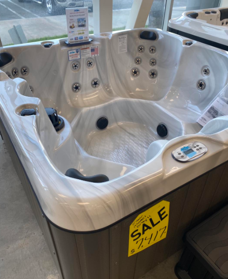 A marbled white hot tub with dark gray siding sits in a showroom, featuring a yellow sale tag reading $7,417.